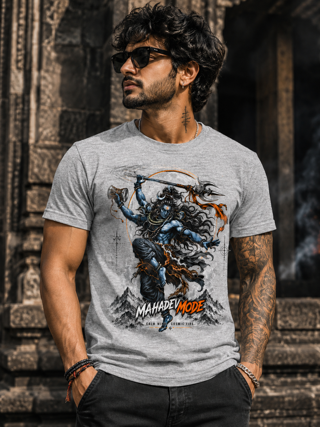 A man wearing a heather gray graphic t-shirt featuring a detailed illustration of Lord Shiva Nataraja and the text 'MAHADEEP MODE'. He is posing outdoors against a dark, textured stone wall.