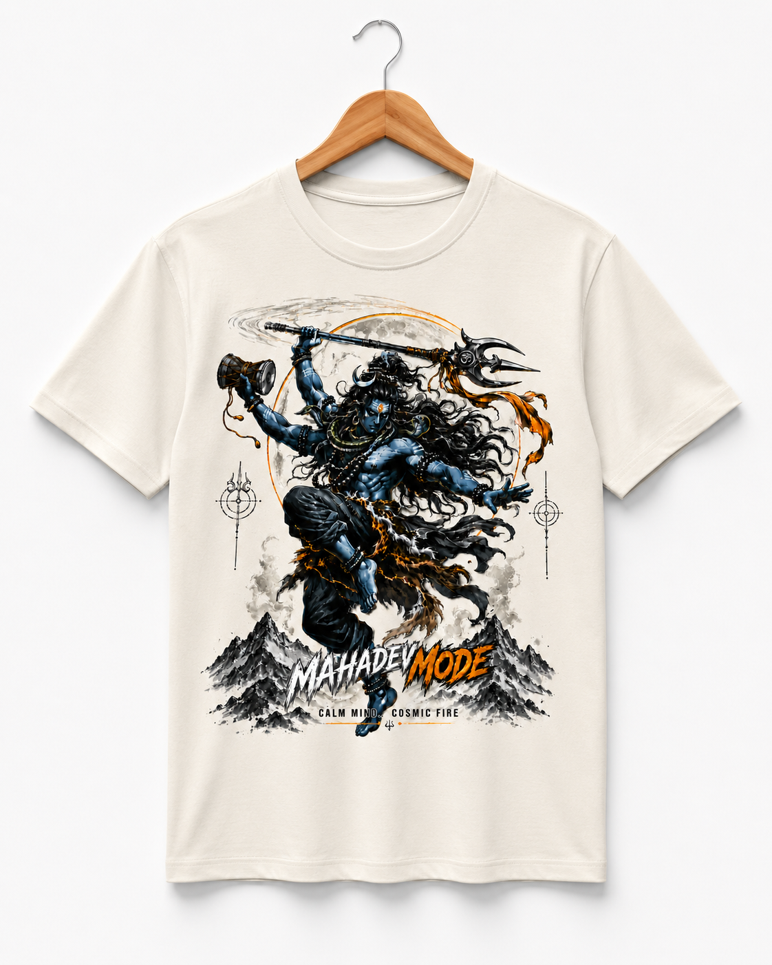An off-white short-sleeve t-shirt hanging on a wooden hanger against a light gray background. The shirt features a large graphic print of a blue-skinned warrior with a trident and mace, set against a mountainous background with the text 'MAHADEVI MODE' and 'CALM ANXIETY COSMIC FUE'.