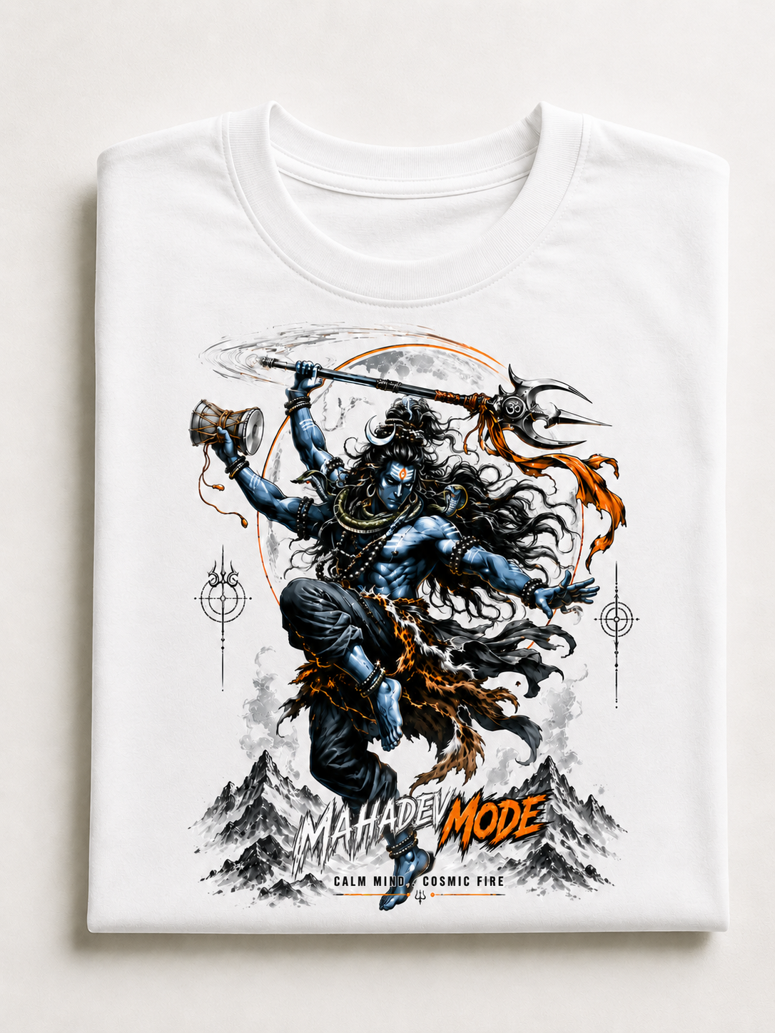 A folded white crewneck t-shirt featuring a detailed graphic print of a Hindu deity with long black hair, holding a trident and a mace, set against a mountainous background with orange and black text reading 'MAHADEI MODE'.