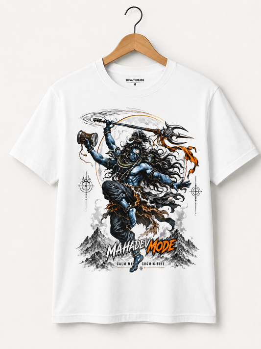 A white short-sleeve graphic T-shirt hanging on a wooden hanger against a light beige wall. The shirt features a large front print of a blue-skinned warrior holding weapons, with the text 'MAHADEV MODE' and 'CALM WITHOUT FIRE' in black and orange.